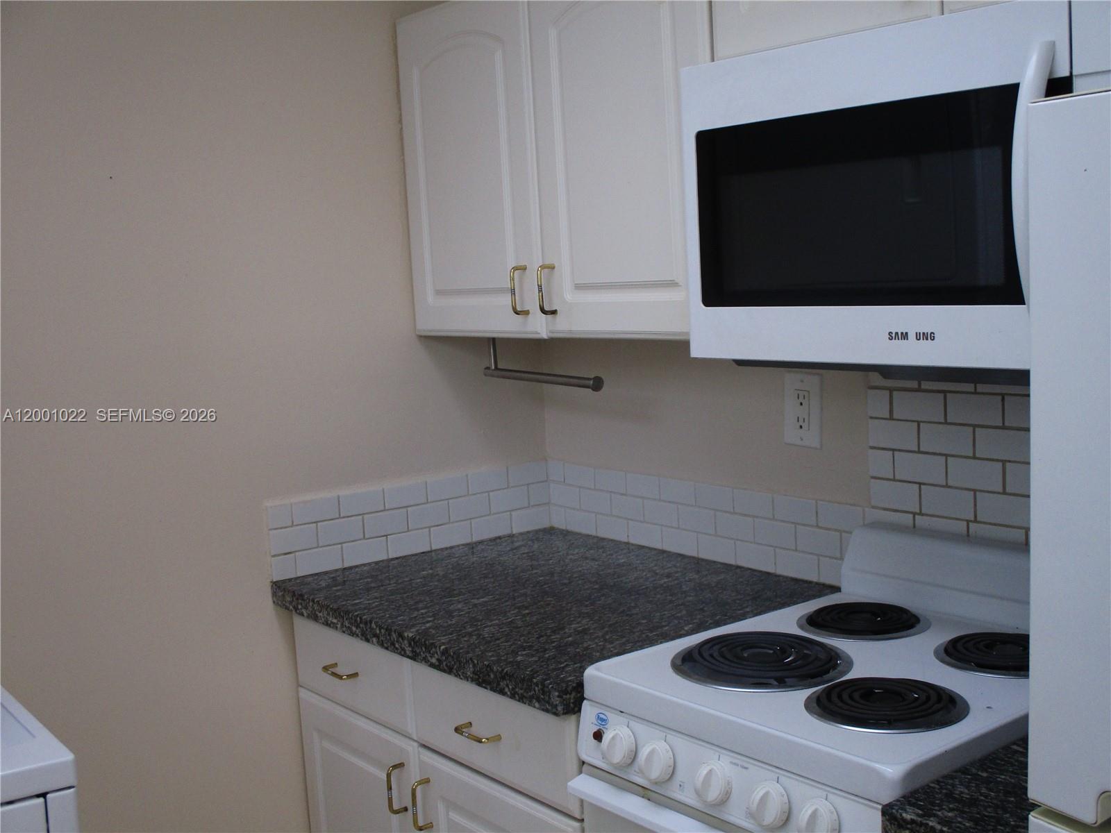 A kitchen features white cabinets, a dark granite countertop, a white stove, and a microwave — 1949 Taylor St # 9, Hollywood FL 33020, HOLLYWOOD, FL