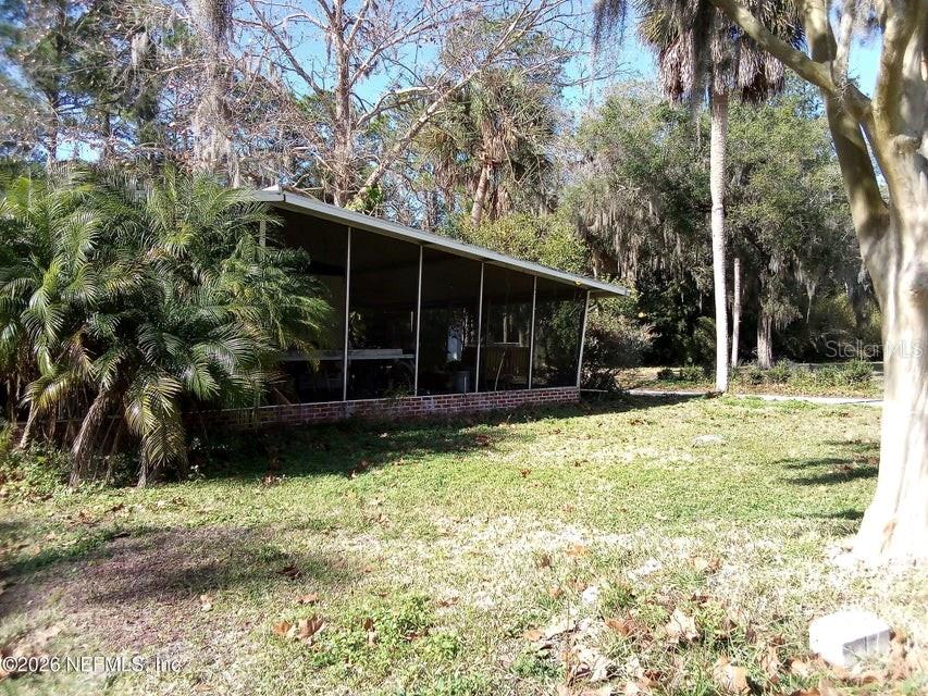 A screened-in porch with a brick base sits in a yard with mature trees — 101 S GERALDO ROAD, EAST PALATKA, FL