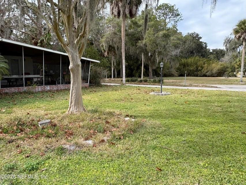 A grassy yard features a large tree, a screened-in porch, and a lamp post — 101 S GERALDO ROAD, EAST PALATKA, FL