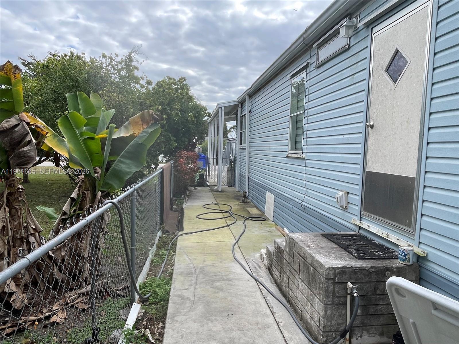 A concrete walkway runs along the side of a blue-sided house with a metal door — 19800 SW 180th Ave UNIT 132, Miami FL 33187, MIAMI, FL