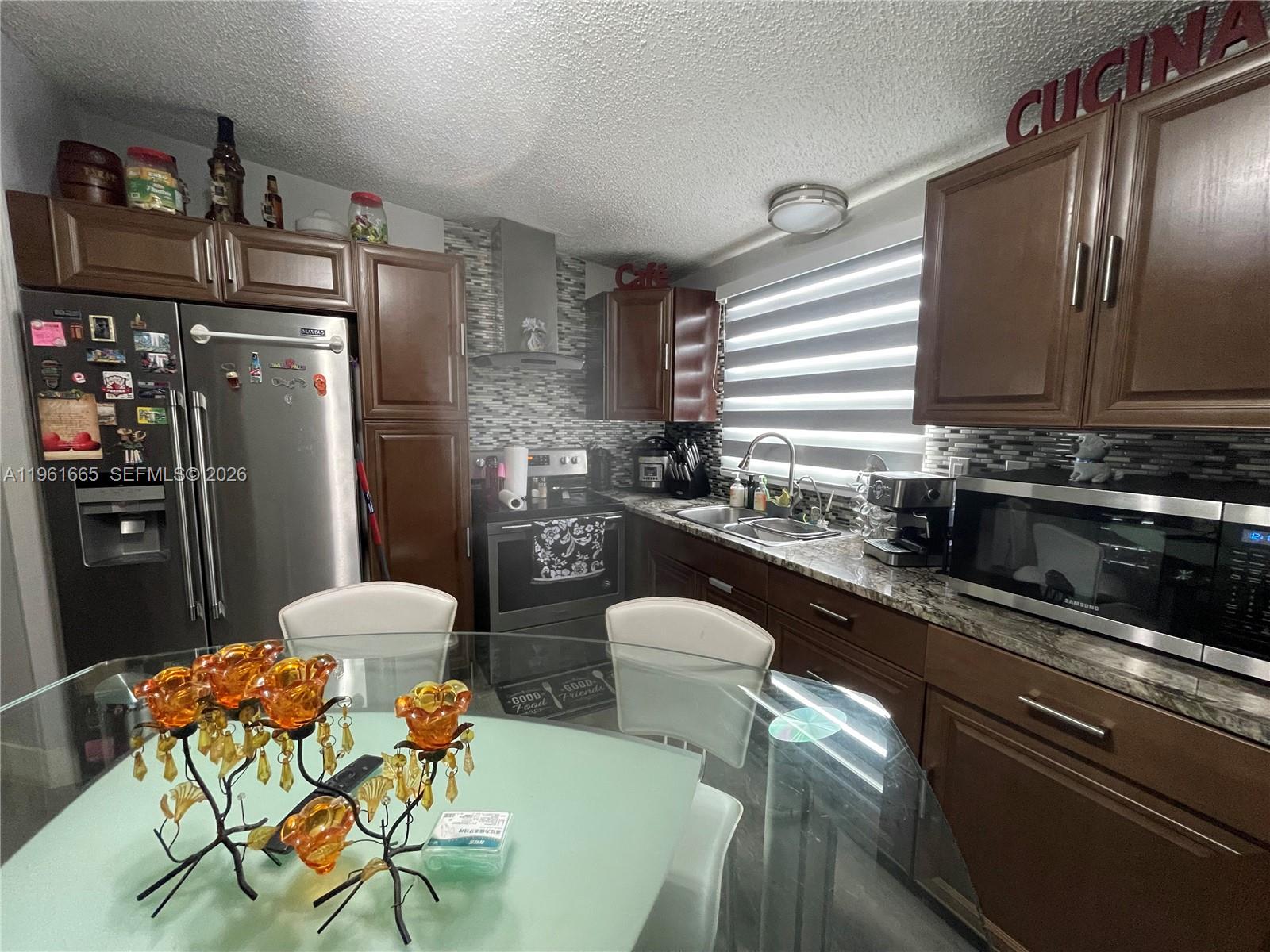 A kitchen features dark wood cabinets, stainless steel appliances, a glass table, and tiled backsplash — 19800 SW 180th Ave UNIT 132, Miami FL 33187, MIAMI, FL