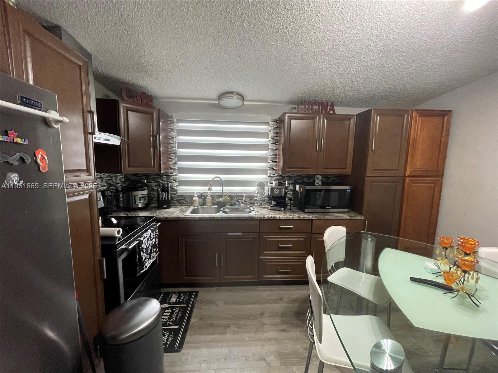 A kitchen features dark wood cabinets, stainless steel appliances, and a glass dining table — 19800 SW 180th Ave UNIT 132, Miami FL 33187, MIAMI, FL