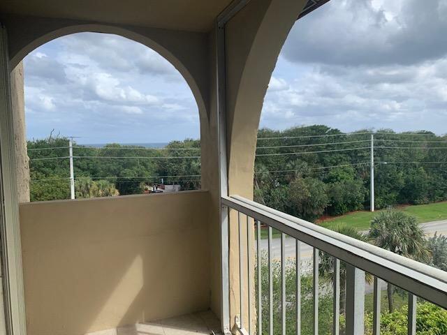 A balcony with an arched opening overlooks a road, trees, and a distant ocean view — 950 Ponce De Leon Road # 5010, Boca Raton FL 33432, BOCA RATON, FL