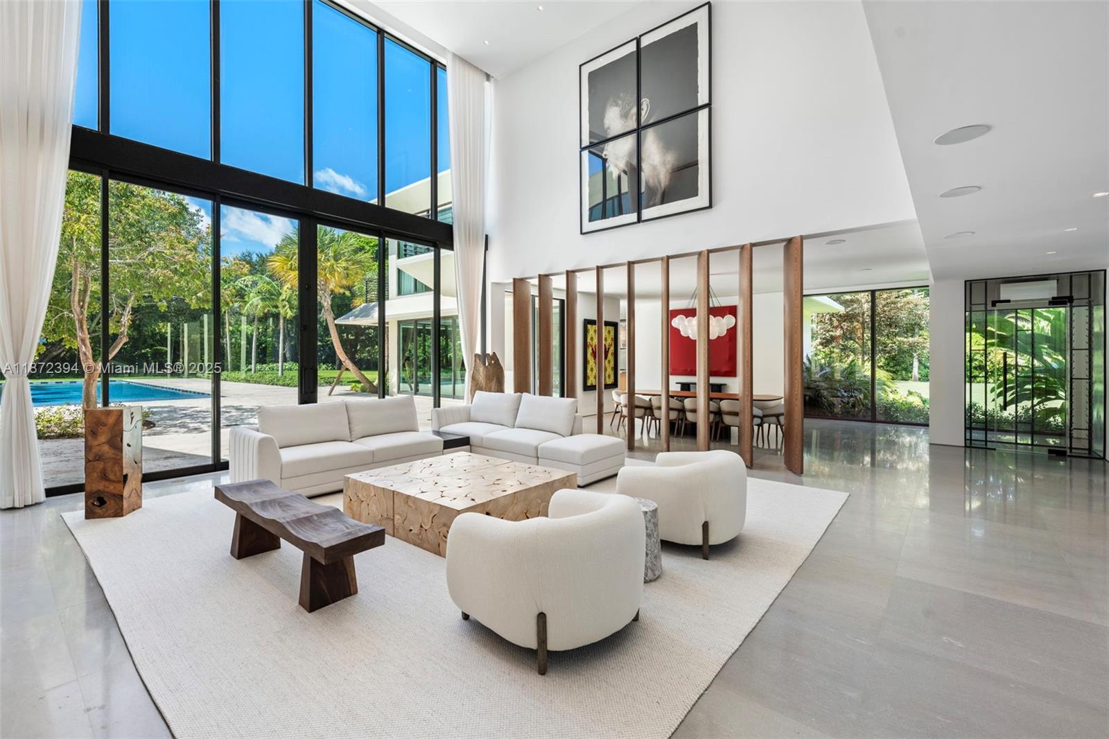 A bright, modern living room features floor-to-ceiling windows, white sofas, and a wooden coffee table — 9440 Old Cutler Ln, Coral Gables FL 33156, CORAL GABLES, FL