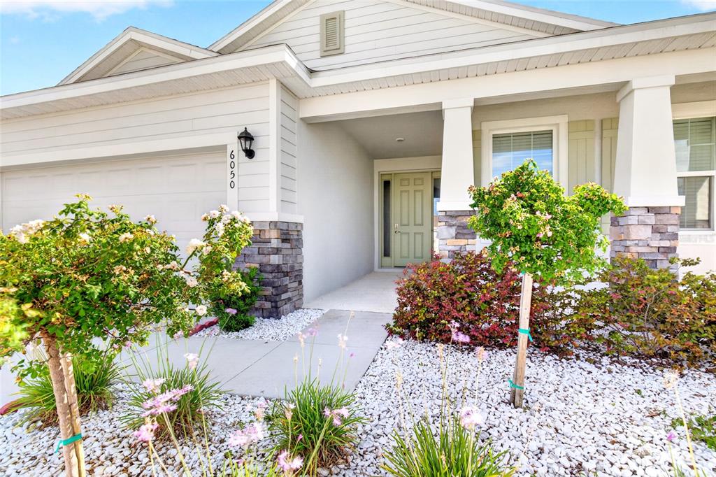 A single-story house exterior features a stone-accented facade, a covered entryway, and landscaped front yard — 6050 SW 93RD LOOP, OCALA, FL