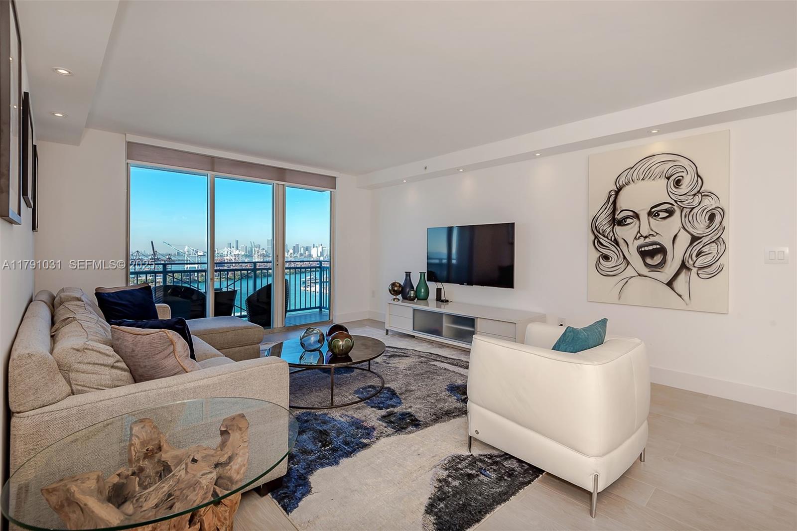A modern living room features a sectional sofa, white armchair, television, and a balcony view — 90 Alton Rd # 2410, Miami Beach FL 33139, MIAMI BEACH, FL