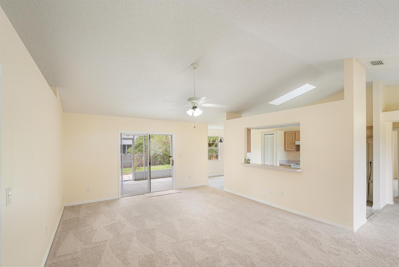 A living room with beige carpet, cream walls, a ceiling fan, and a kitchen pass-through — 1545 Barber Street, Sebastian FL 32958, SEBASTIAN, FL