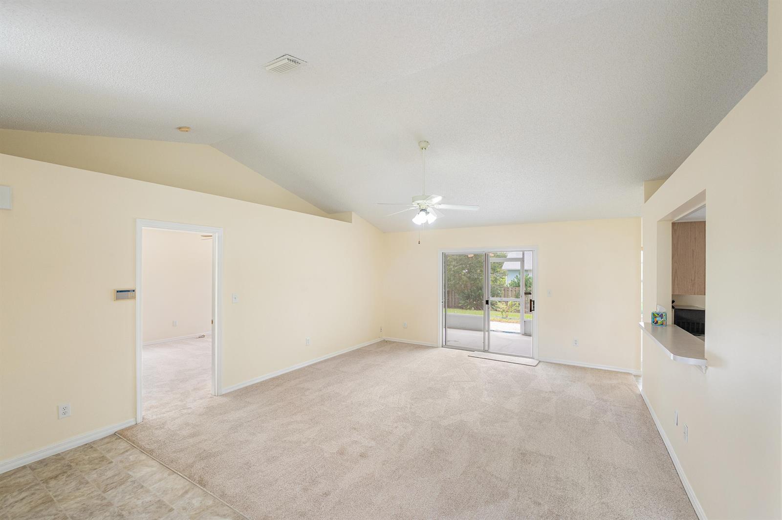 A living room with beige carpet, vaulted ceilings, a ceiling fan, and sliding glass doors — 1545 Barber Street, Sebastian FL 32958, SEBASTIAN, FL
