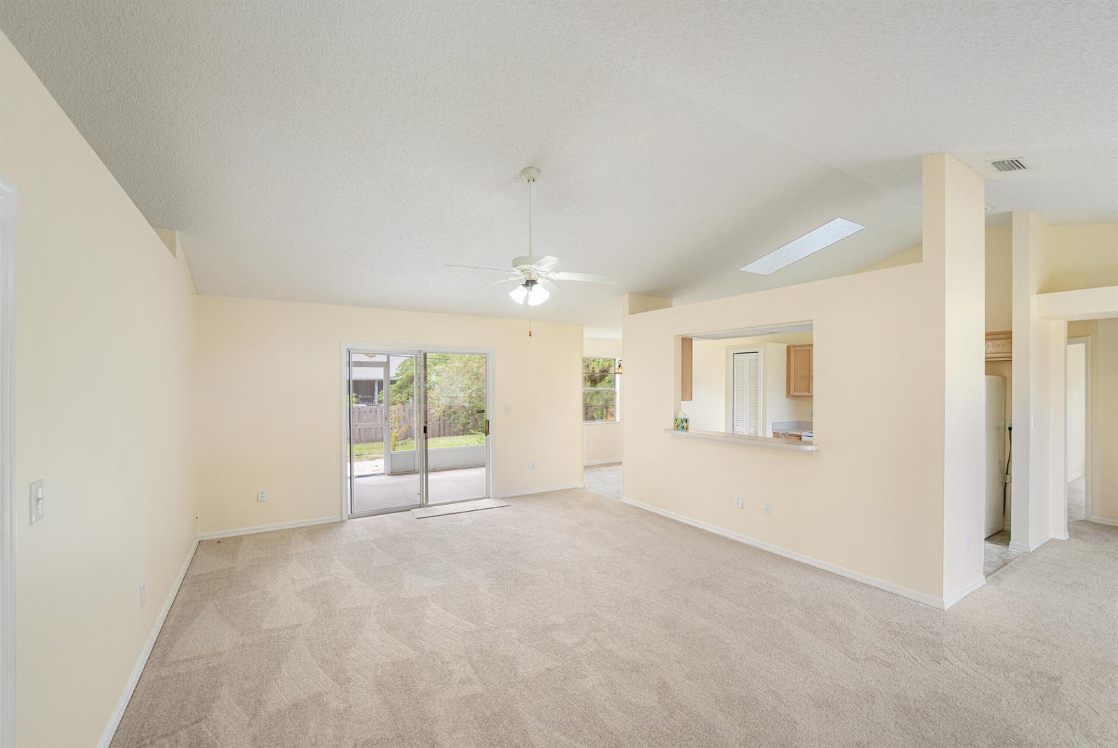A living room with beige carpet, vaulted ceilings, a ceiling fan, and a kitchen pass-through — 1545 Barber Street, Sebastian FL 32958, SEBASTIAN, FL