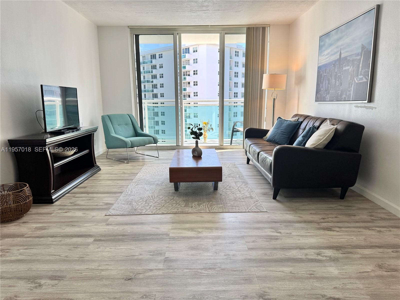A living room features a dark leather sofa, wood coffee table, and gray wood-look flooring — 3000 S OCEAN DR # 1006, Hollywood FL 33019, HOLLYWOOD, FL