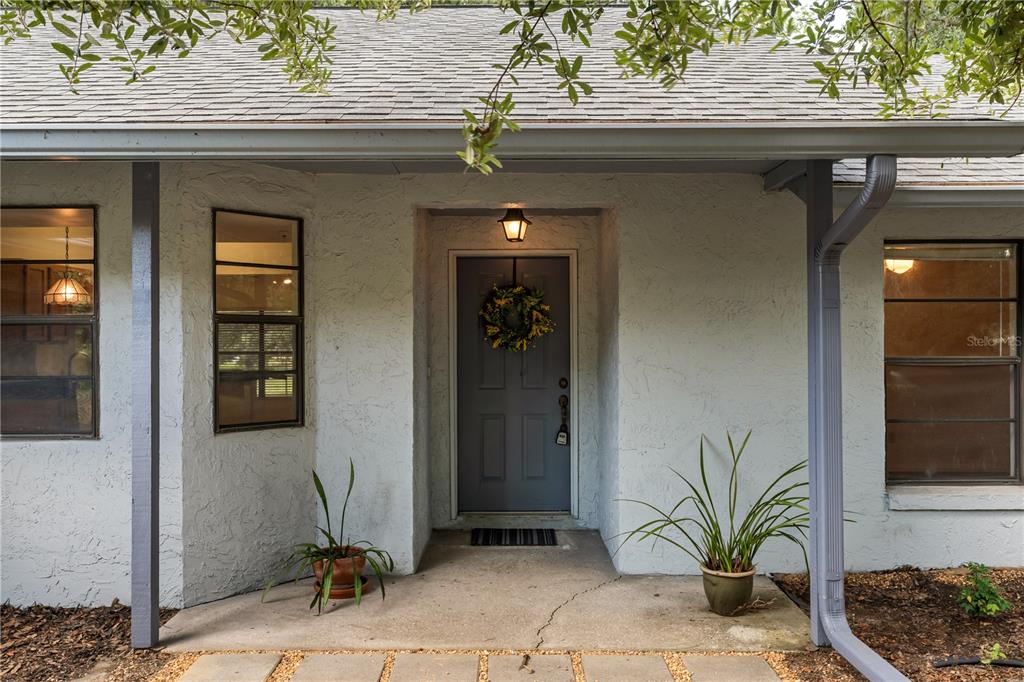 The front exterior of a house features a gray door, a wreath, and two potted plants — 16104 SANDHILL ROAD, WINTER GARDEN, FL