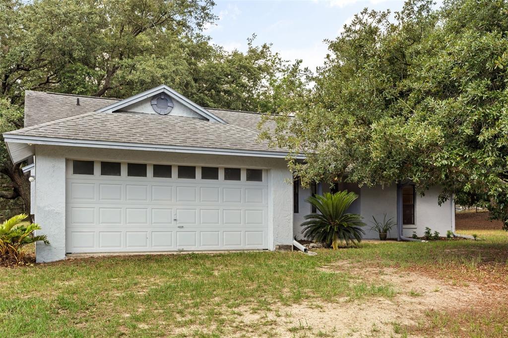 A single-story house with a white garage door, light-colored stucco siding, and surrounding trees — 16104 SANDHILL ROAD, WINTER GARDEN, FL