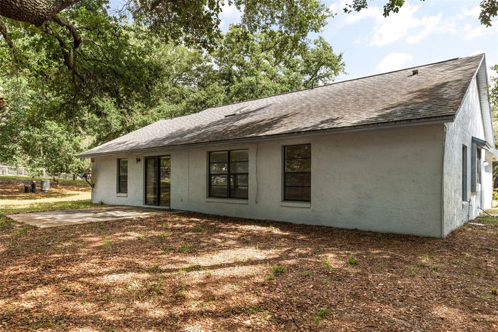 The exterior of a single-story house with white stucco walls and a concrete patio — 16104 SANDHILL ROAD, WINTER GARDEN, FL