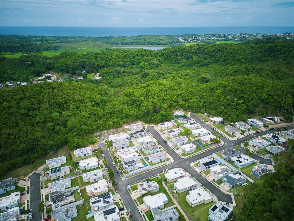 An aerial view shows a residential neighborhood nestled against a dense, green forest and coastline — PR 616 LA MONSERRATE, MANATI, PR