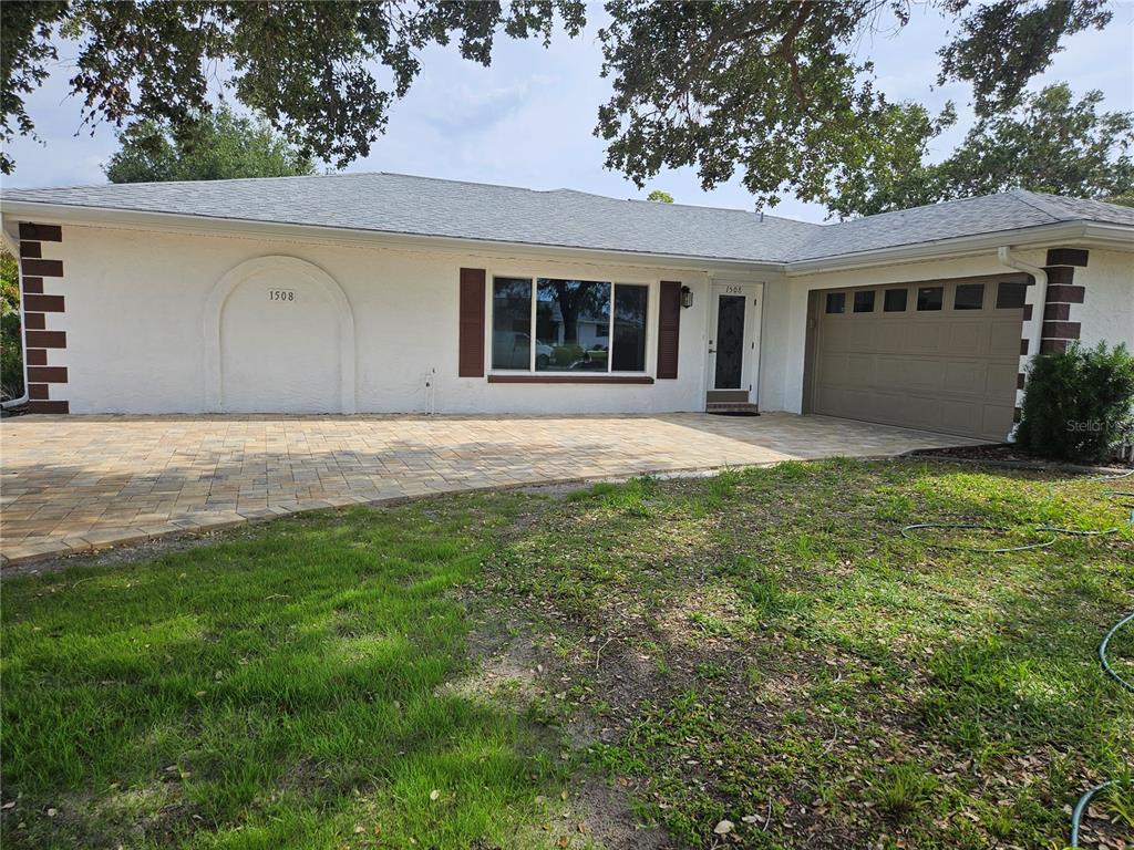 A single-story house with a white stucco facade, brown shutters, and a paved driveway — 1508 FLAMINGO LANE, SUN CITY CENTER, FL