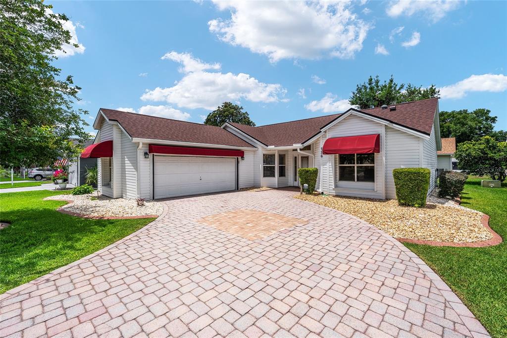 A single-story house with white siding, red awnings, and a paved driveway under a blue sky — 736 CORTEZ AVENUE, THE VILLAGES, FL