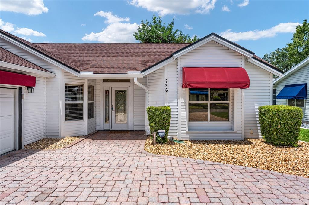 A single-story house with white siding, a red awning, and a brick paver driveway — 736 CORTEZ AVENUE, THE VILLAGES, FL