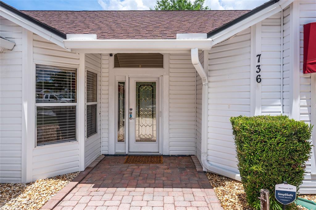 The exterior of a house features white siding, a brick walkway, and a glass-paneled door — 736 CORTEZ AVENUE, THE VILLAGES, FL