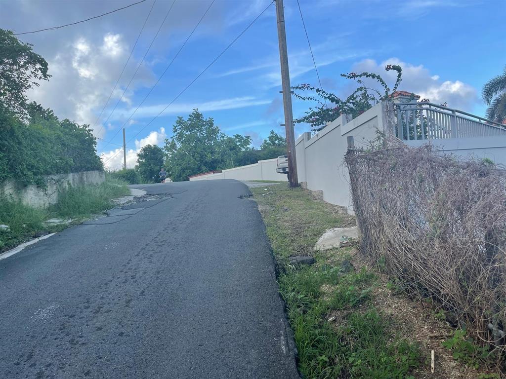A paved road leads uphill past a white wall and a chain-link fence — 3 CANDELERO UNIT 1, HUMACAO, PR