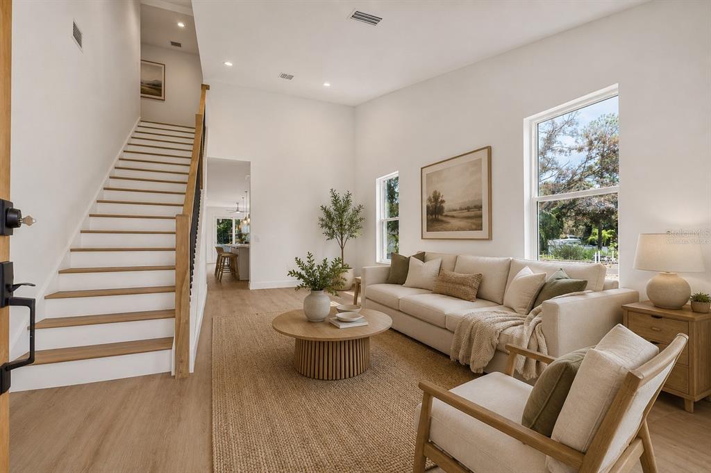 A bright living room features a staircase, a beige sofa, and a round wooden coffee table — 7617 ALVINA STREET, TAMPA, FL