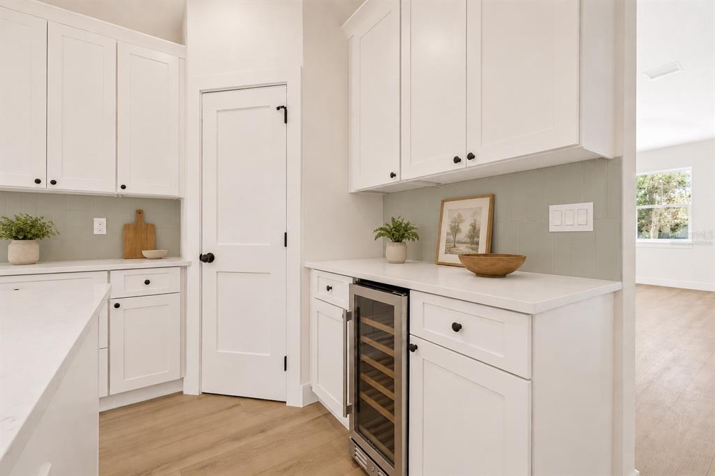 A kitchen features white cabinets, a wine cooler, light countertops, and a sage green backsplash — 7617 ALVINA STREET, TAMPA, FL