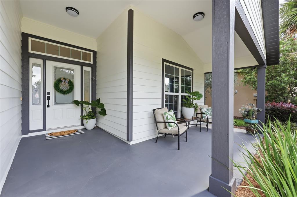 A covered front porch with white siding, dark trim, two chairs, and a front door — 14594 NW 25TH AVENUE, NEWBERRY, FL