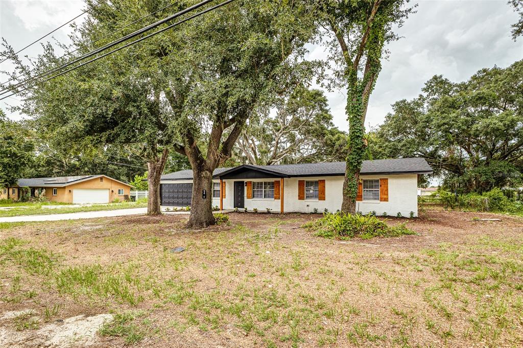 A white brick, single-story house with a dark roof and wooden shutters sits among trees — 5421 LAKE LUTHER ROAD, LAKELAND, FL