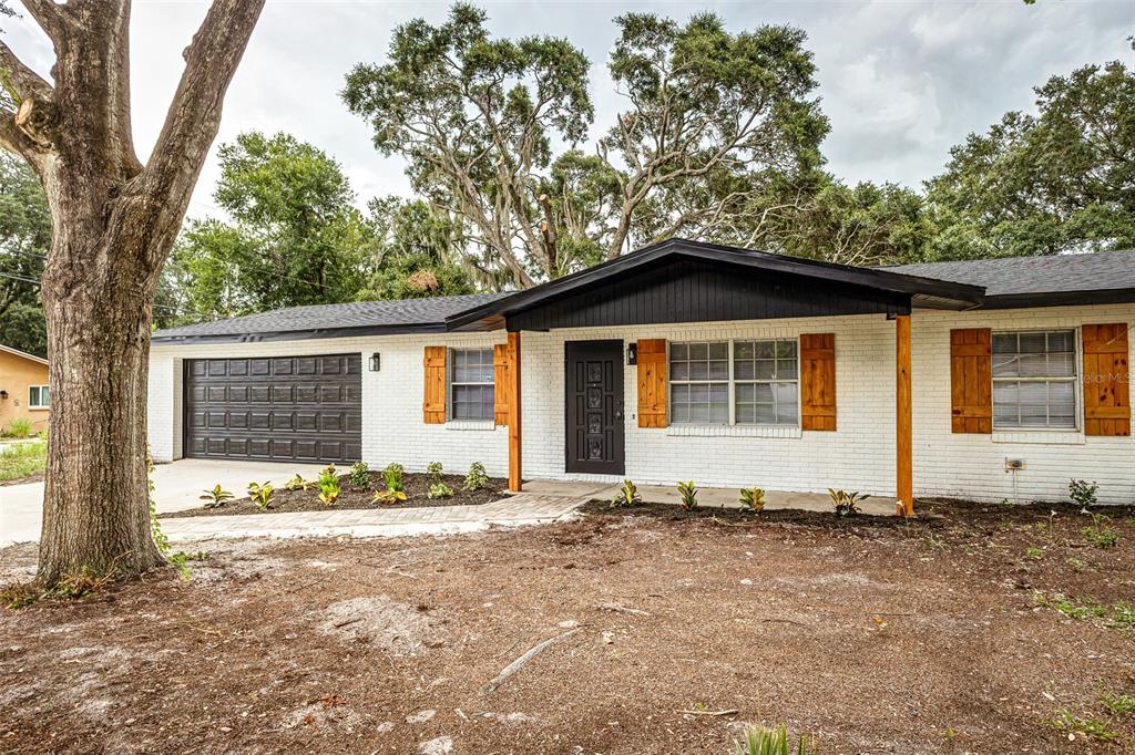 A single-story white brick house with a dark garage door and wooden shutters — 5421 LAKE LUTHER ROAD, LAKELAND, FL