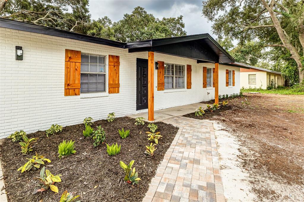 A white brick house features wooden shutters, a black front door, and a paver walkway — 5421 LAKE LUTHER ROAD, LAKELAND, FL