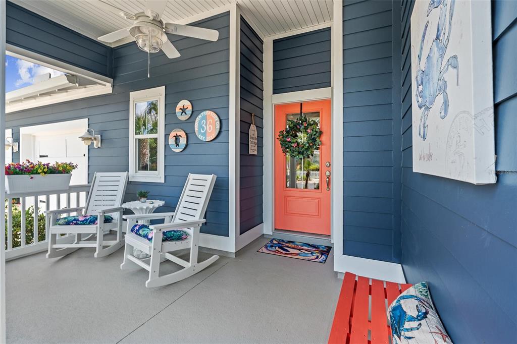 A blue-sided porch features a coral front door, two white rocking chairs, and a bench — 36 HIDDEN TREASURE DRIVE, PALM COAST, FL