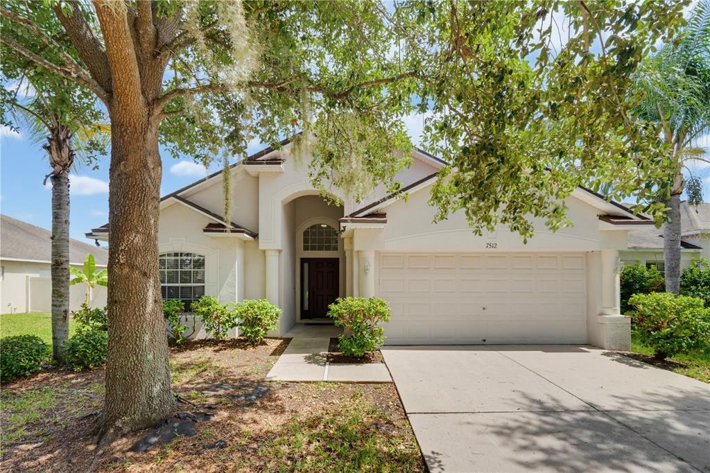 A single-story house with a beige stucco exterior, a two-car garage, and a large tree — 7512 TURTLE VIEW DRIVE, RUSKIN, FL