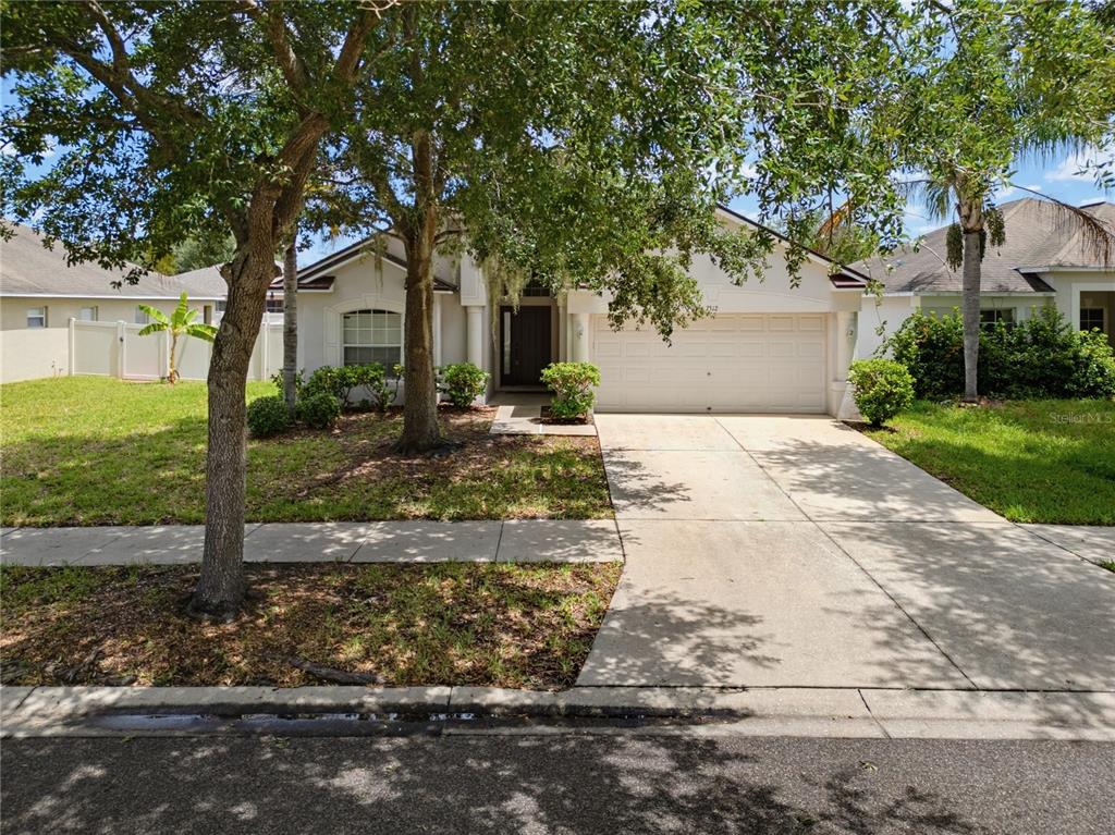 A single-story house with a white garage, a concrete driveway, and trees in the yard — 7512 TURTLE VIEW DRIVE, RUSKIN, FL