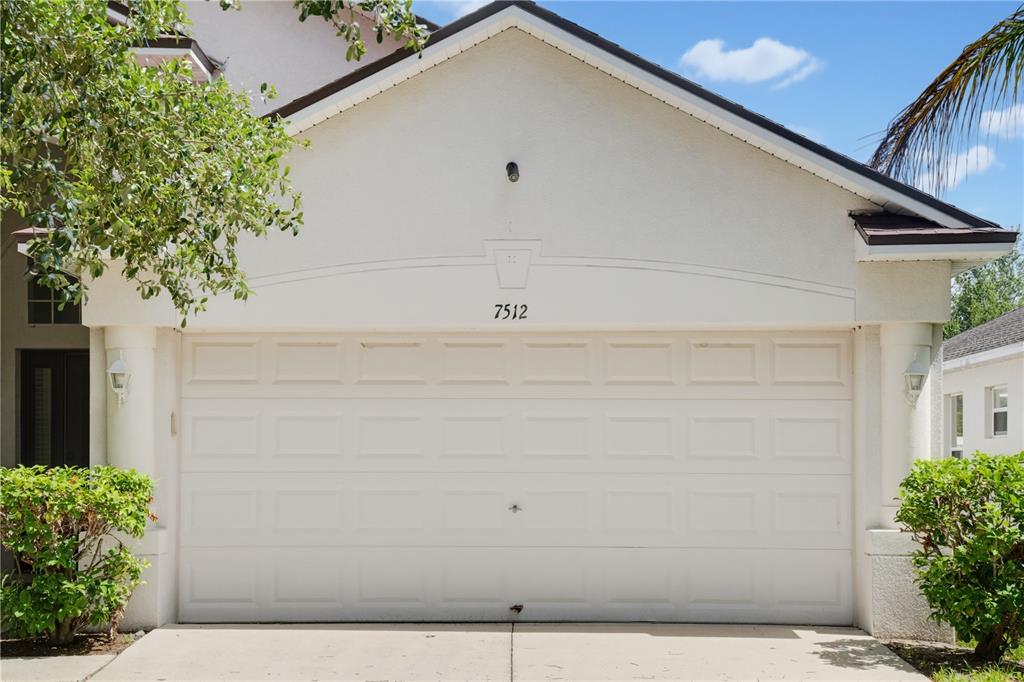 A white two-car garage door with a house number above it on a stucco home — 7512 TURTLE VIEW DRIVE, RUSKIN, FL