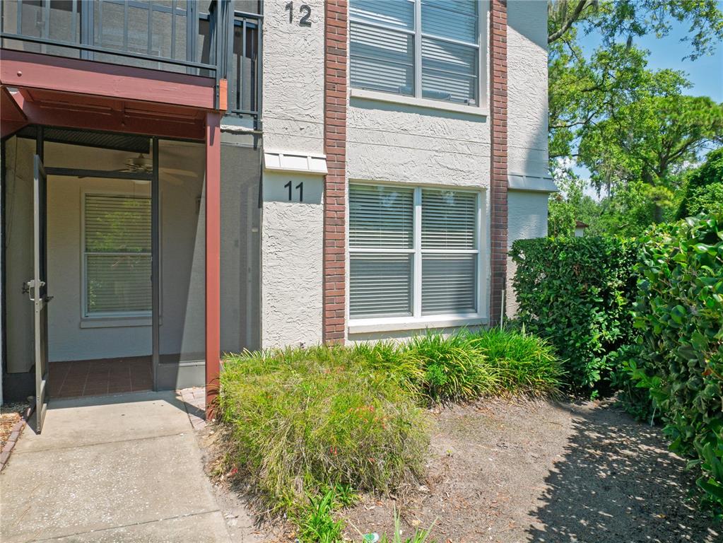 An exterior view of a ground-floor apartment entrance with a screened porch and brick accents — 3455 COUNTRYSIDE BOULEVARD UNIT 11, CLEARWATER, FL