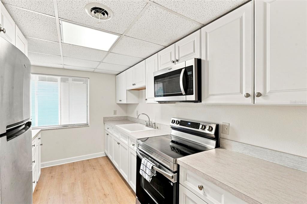 A galley kitchen features white cabinets, stainless steel appliances, and light wood-look flooring — 4435 1ST STREET NE UNIT 110, ST PETERSBURG, FL