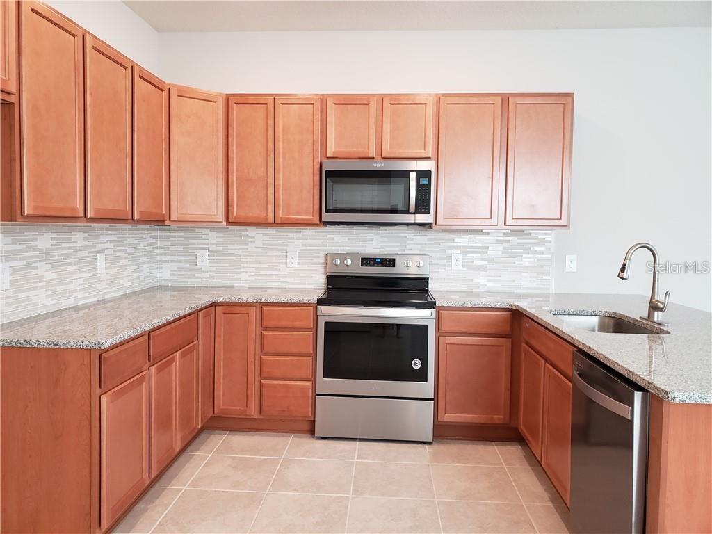A kitchen features light wood cabinets, granite countertops, stainless steel appliances, and a tiled backsplash — 2659 MEAD AVENUE, ST CLOUD, FL