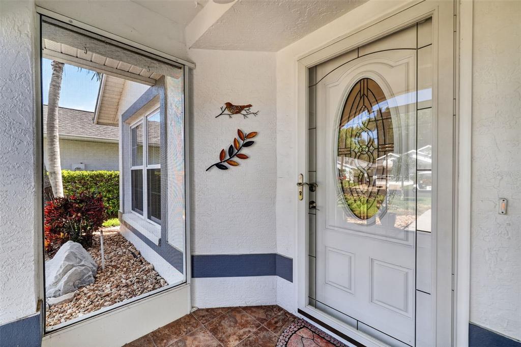 A white front door with an oval glass insert sits beside a screened-in porch area — 4431 FERN DRIVE, BRADENTON, FL