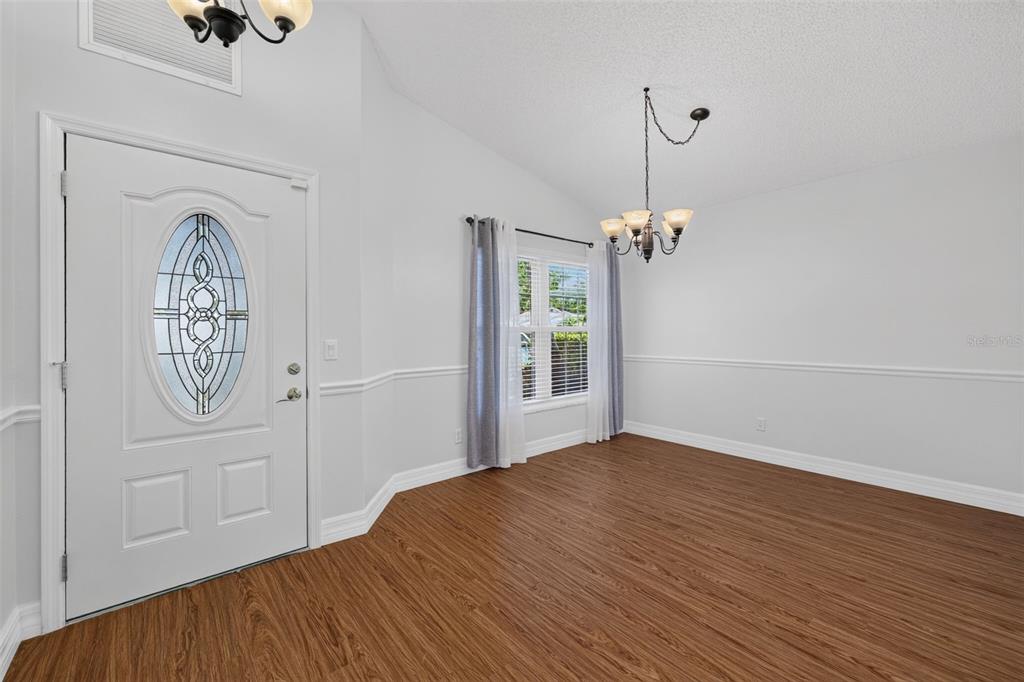 An empty room with wood-look flooring, white walls, a front door, and a chandelier — 4431 FERN DRIVE, BRADENTON, FL