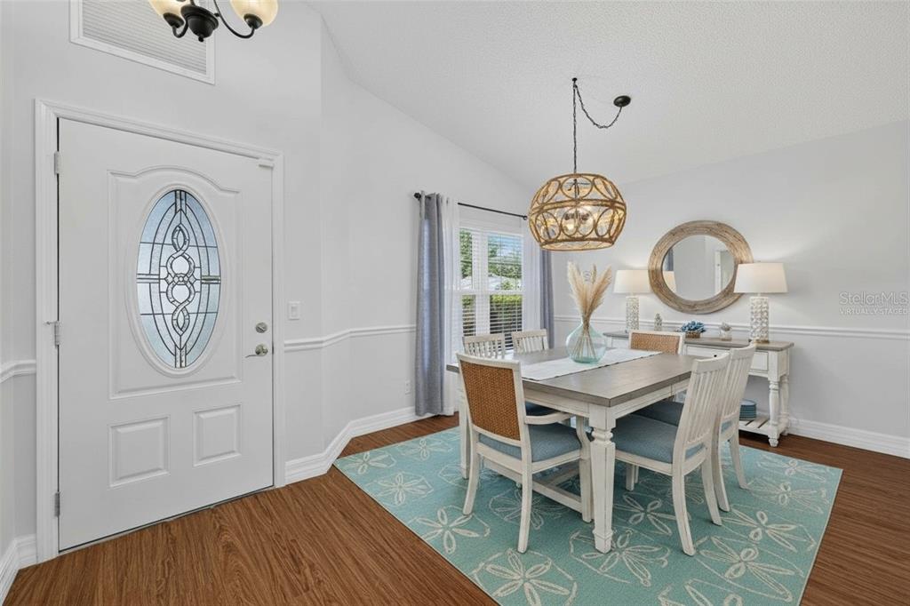 A dining room features a wooden table, blue chairs, a patterned rug, and a front door — 4431 FERN DRIVE, BRADENTON, FL