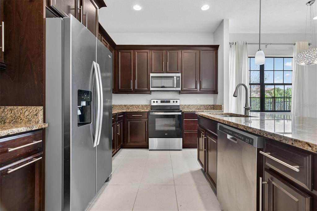 A kitchen with dark wood cabinets, granite countertops, stainless steel appliances, and tile flooring — 10429 STAPELEY DR, ORLANDO, FL
