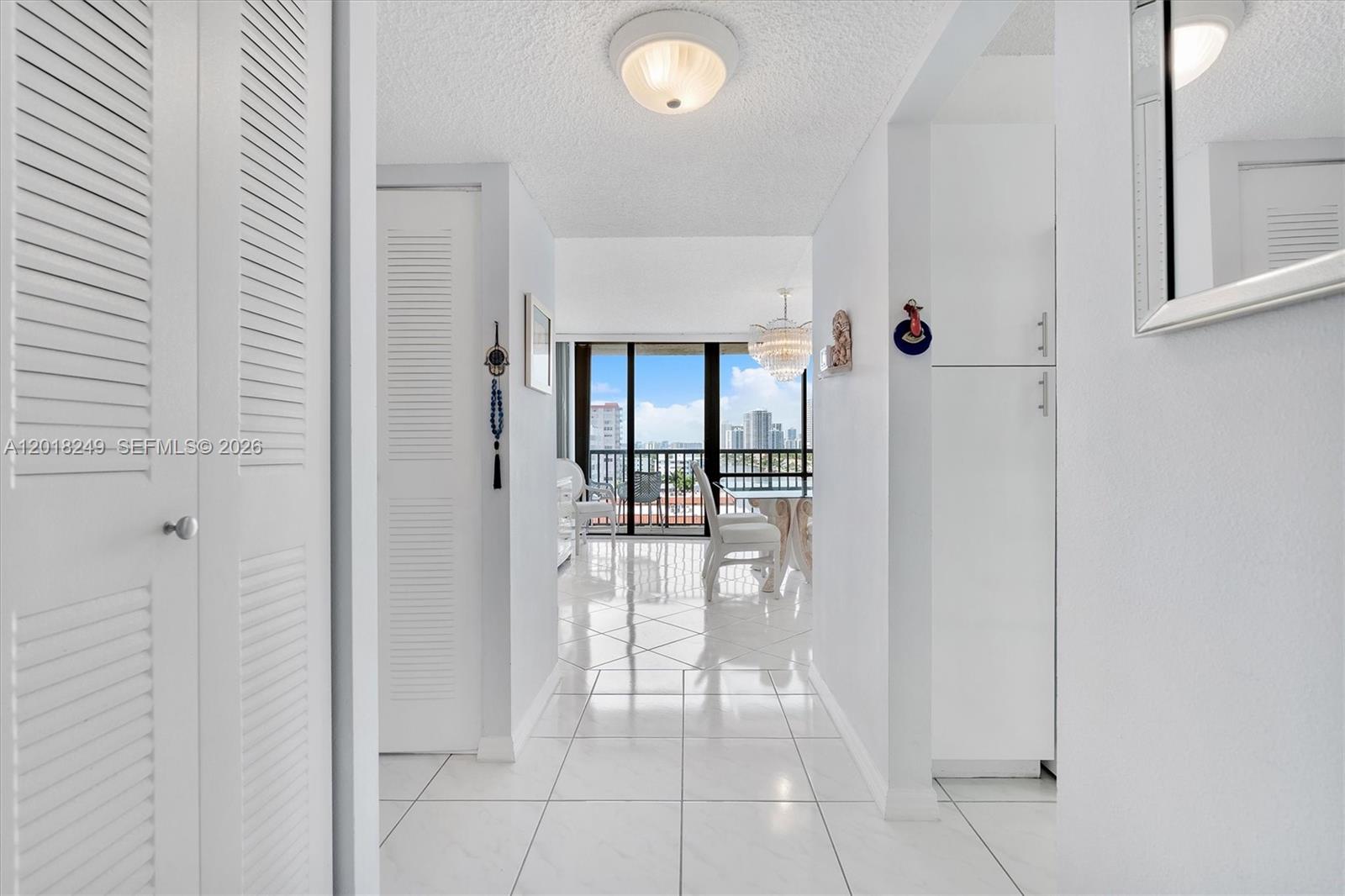 A white hallway with tiled floors leads to a dining area with a balcony view — 2017 S Ocean Dr # 910, Hallandale Beach FL 33009, HALLANDALE BEACH, FL
