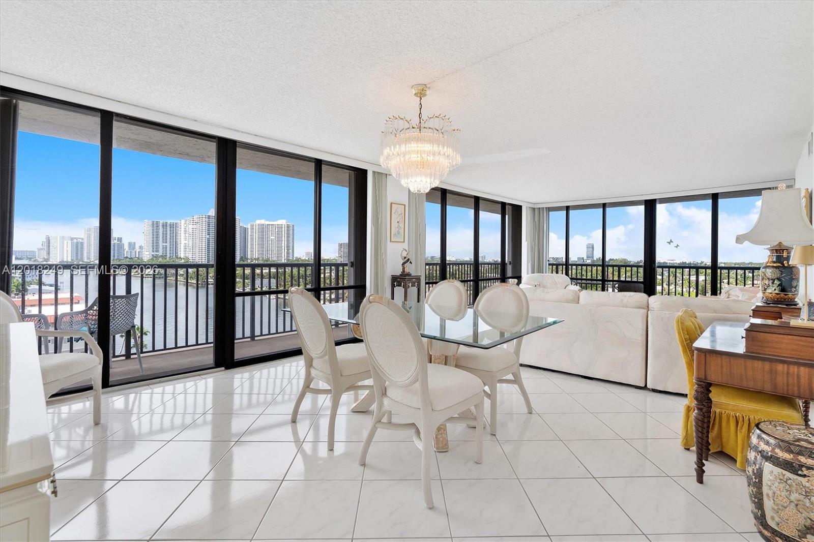 A dining area with a glass table, chandelier, and floor-to-ceiling windows overlooking a city skyline — 2017 S Ocean Dr # 910, Hallandale Beach FL 33009, HALLANDALE BEACH, FL