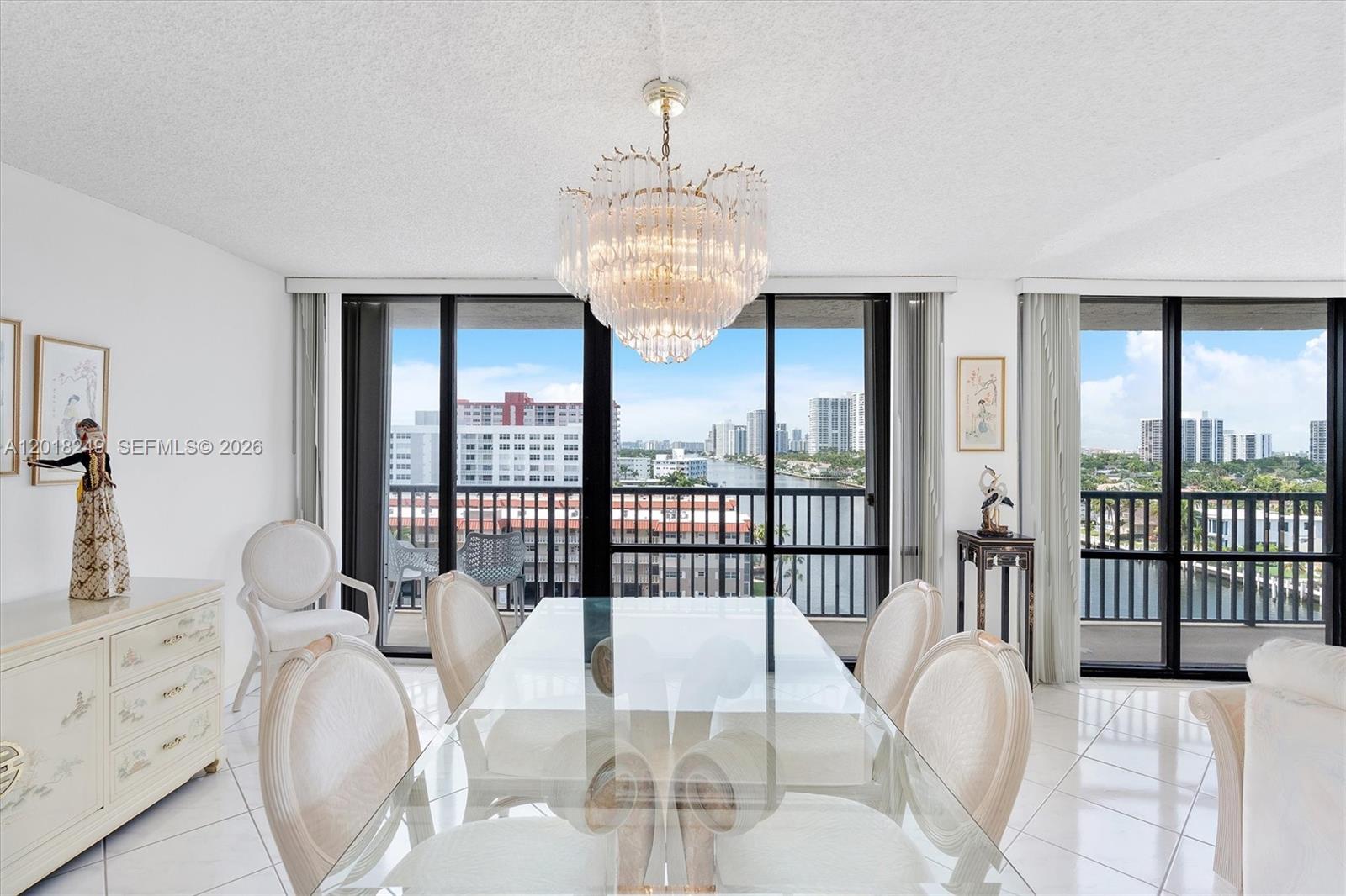 A dining room features a glass table, chandelier, and floor-to-ceiling windows overlooking a waterway — 2017 S Ocean Dr # 910, Hallandale Beach FL 33009, HALLANDALE BEACH, FL