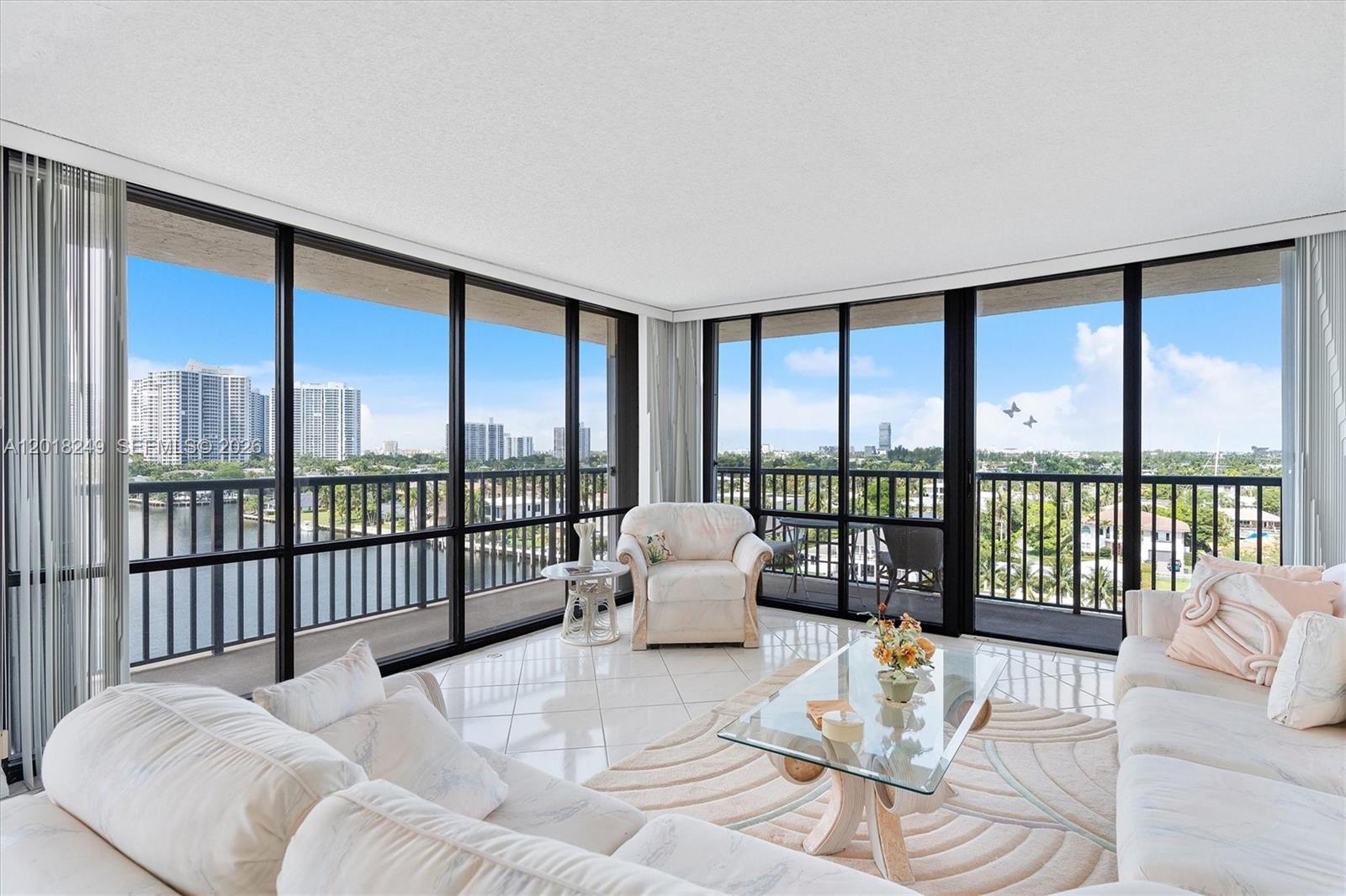 A bright living room features white tile floors, plush furniture, and floor-to-ceiling windows overlooking water — 2017 S Ocean Dr # 910, Hallandale Beach FL 33009, HALLANDALE BEACH, FL