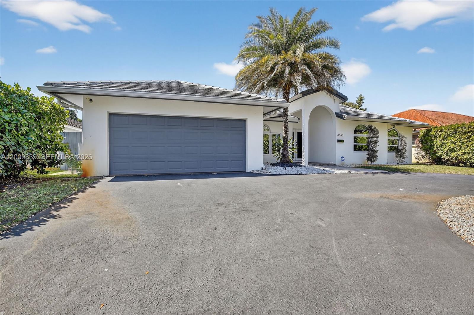 A single-story house with a gray garage door, white stucco walls, and a palm tree — 3540 N Park Rd, Hollywood FL 33021, HOLLYWOOD, FL
