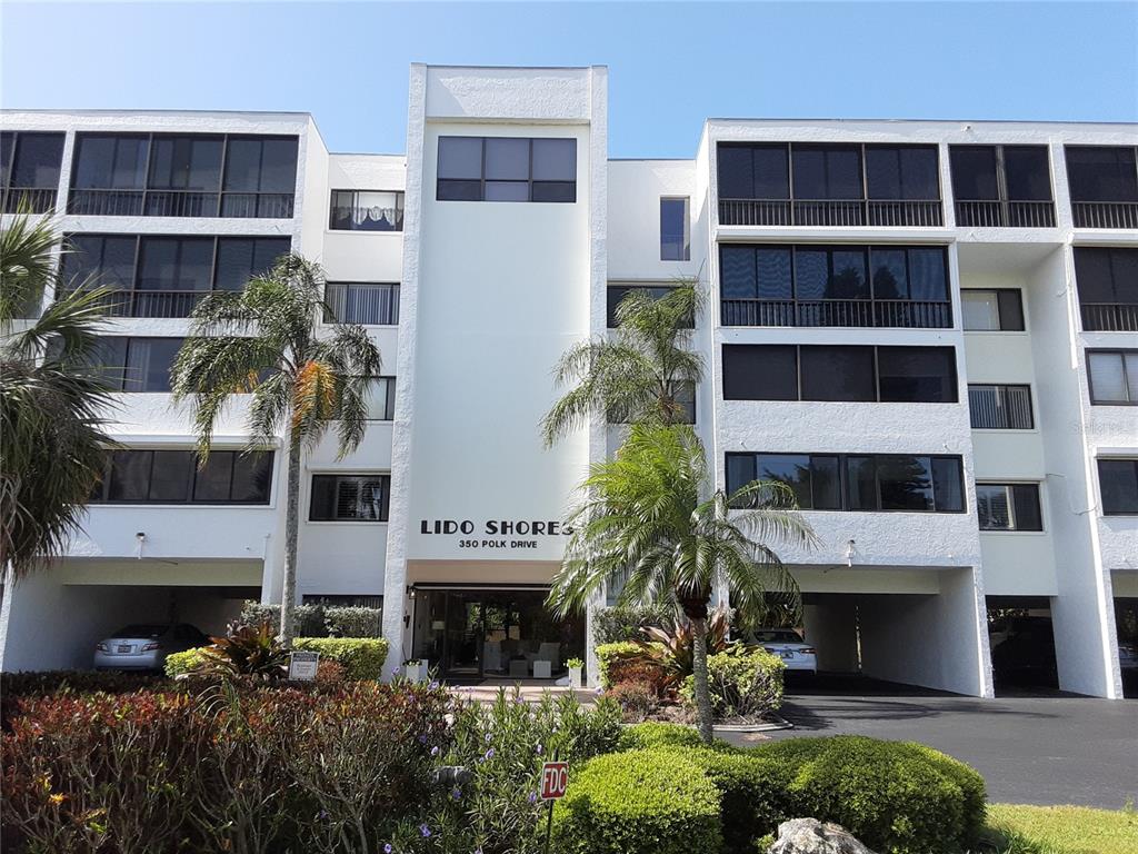 The exterior of a multi-story white apartment building features screened balconies and a ground-level entrance — 350 S POLK DRIVE UNIT 207, SARASOTA, FL