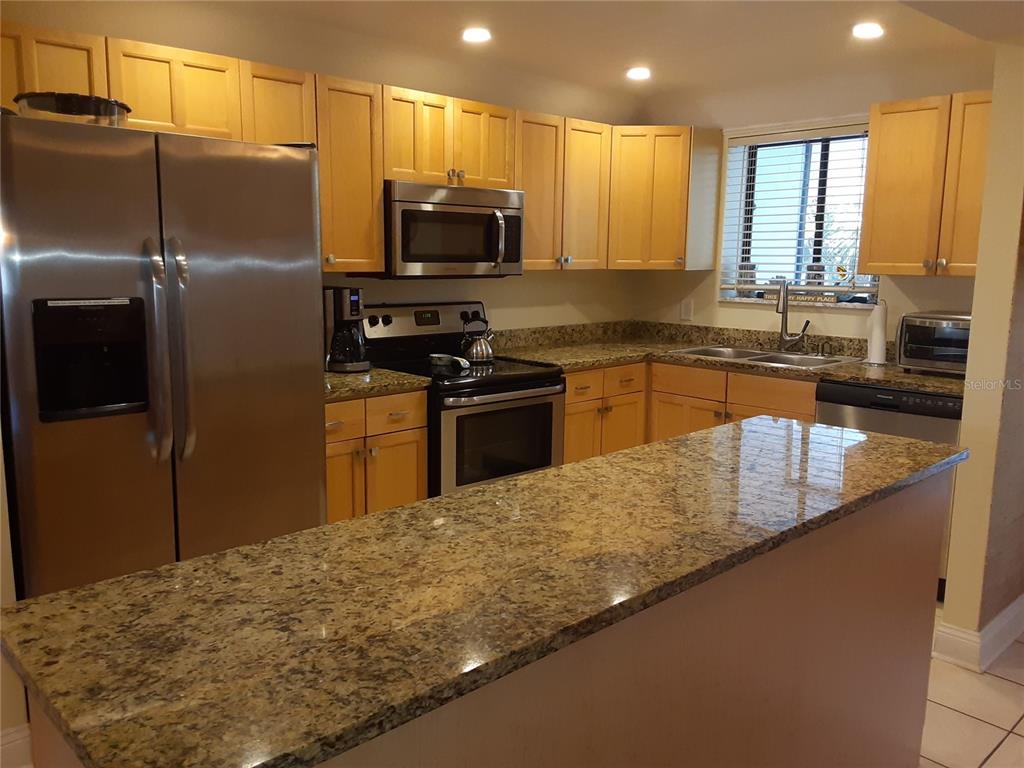 A kitchen features light wood cabinets, granite countertops, stainless steel appliances, and a breakfast bar — 350 S POLK DRIVE UNIT 207, SARASOTA, FL