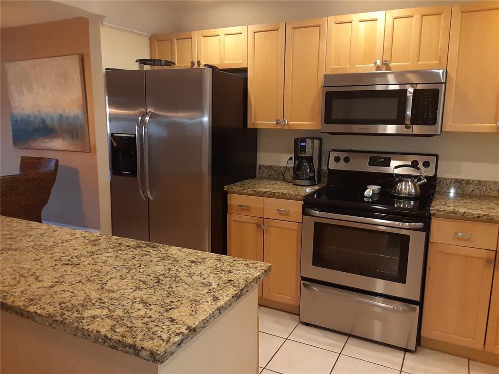 A kitchen features light wood cabinets, stainless steel appliances, and speckled granite countertops — 350 S POLK DRIVE UNIT 207, SARASOTA, FL