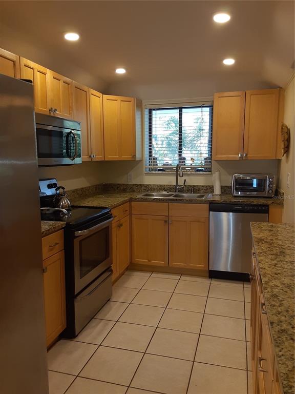A kitchen features light wood cabinets, granite countertops, stainless steel appliances, and tiled flooring — 350 S POLK DRIVE UNIT 207, SARASOTA, FL