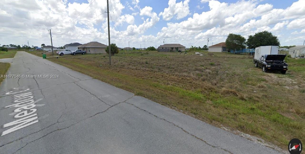 A vacant grassy lot sits along a paved road with houses in the background — 9036 Meadow Terr, La Belle FL 33935, LA BELLE, FL